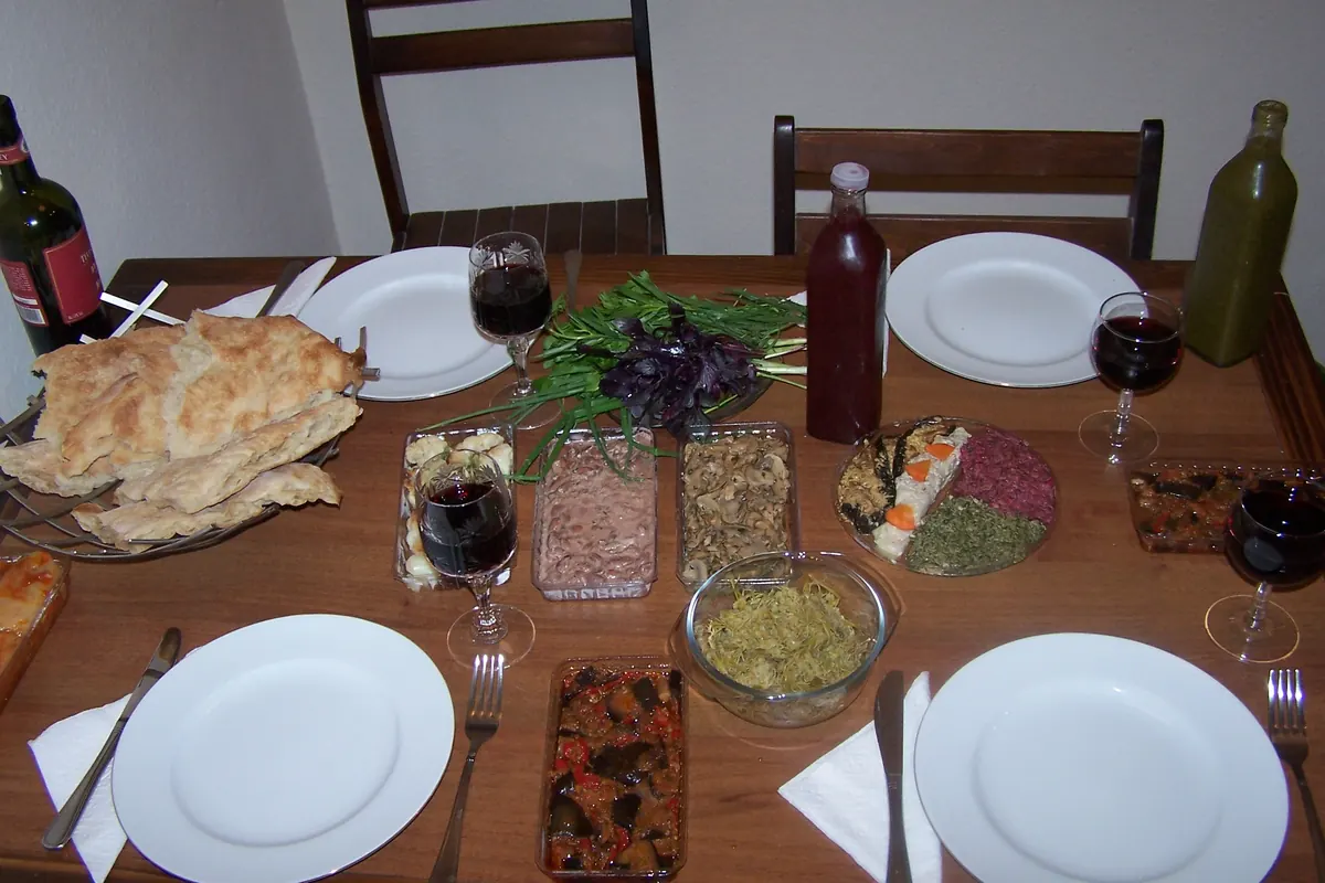 A wooden table laid with plates, glasses of red wine, bread and small dishes of vegetable spreads