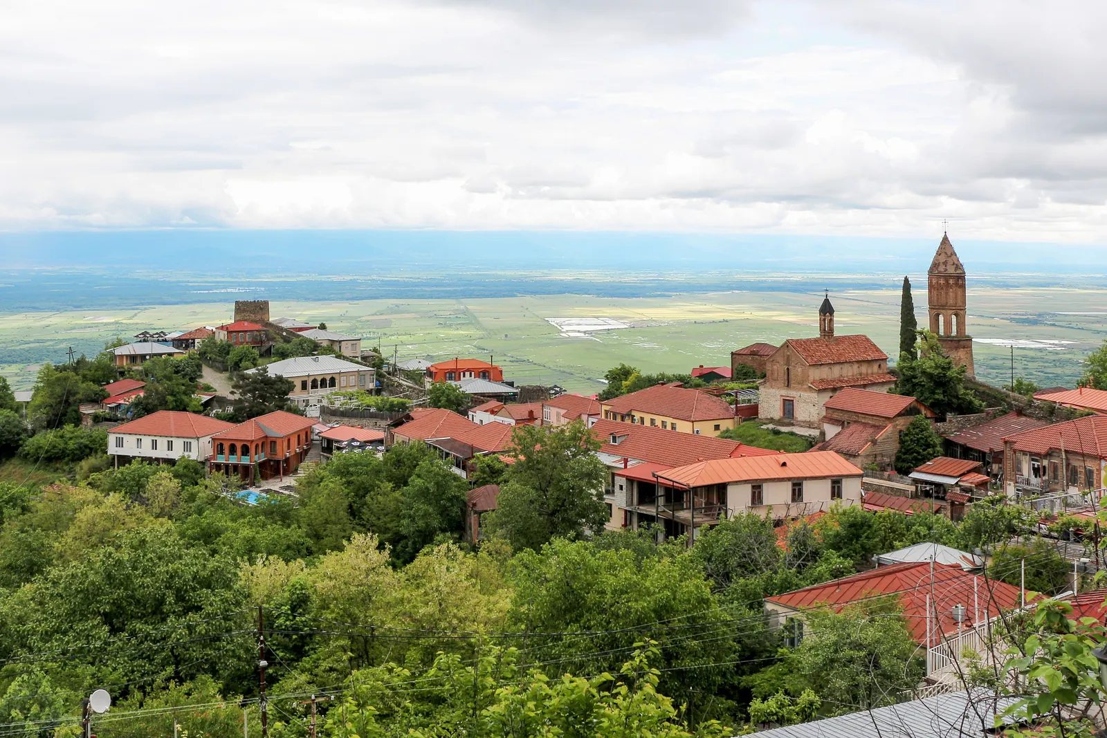Domy s červenými střechami v Sighnaghi na svahu nad širokým údolím Alazani, s věží kostela